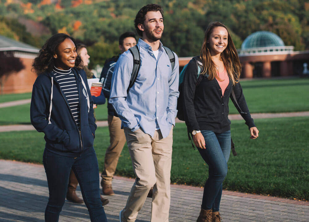 Three students walk across the Quinnipiac quad in the autumn