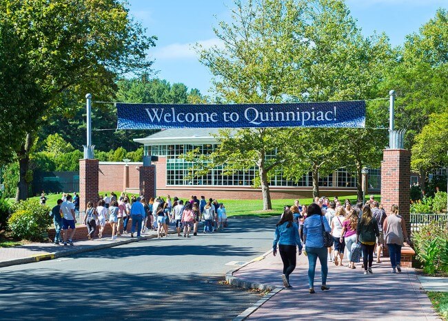 A group of students and their parents walk down Bobcat Way under a "Welcome to Quinnipiac" banner