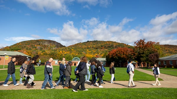 A tour group walks with a Quinnipiac student guide with Sleeping Giant in fall colors behind them