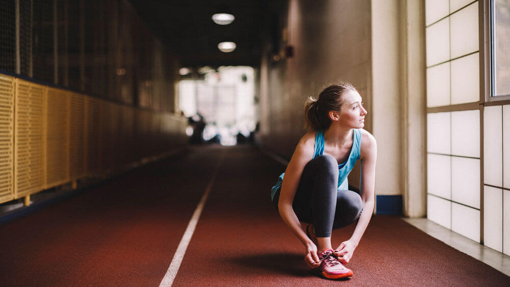 A student takes a quick break to tie her laces while running on the second-floor indoor track at the Athletic and Recreation Center on the Mount Carmel Campus.