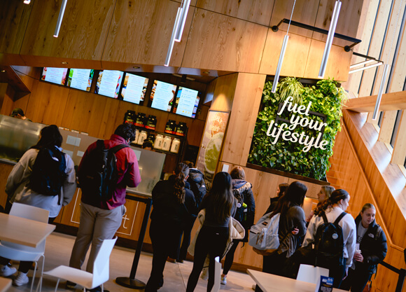 Dozens of students in line outside the Shake Smart, with a wall sign that reads Fuel Your Lifestyle