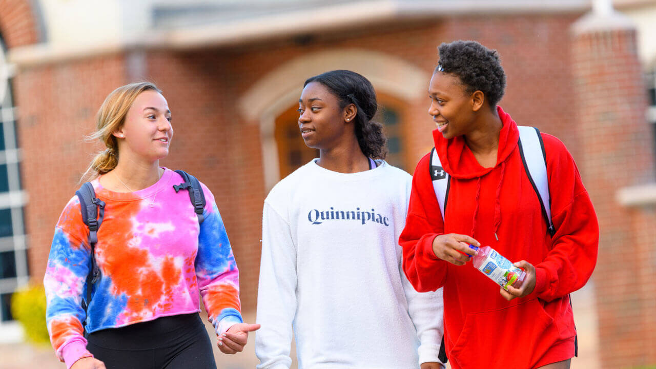 Three students walk across the quad talking together