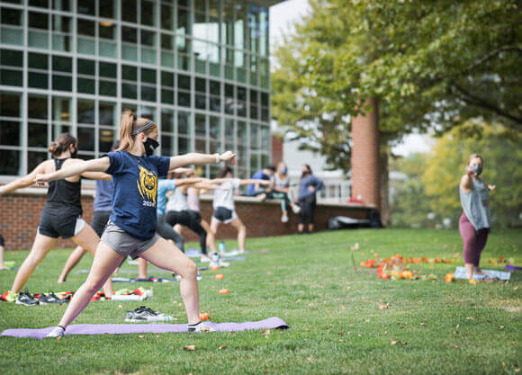 Students wearing face coverings perform outdoor yoga.