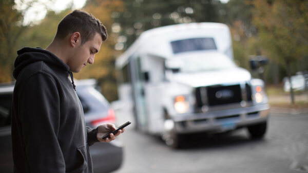 A student uses his mobile phone as a shuttle approaches in the background