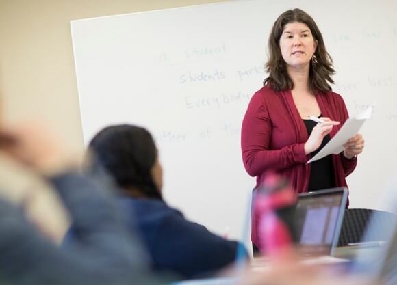 Solomon holds a piece of paper and marker as she speaks in front of a class.