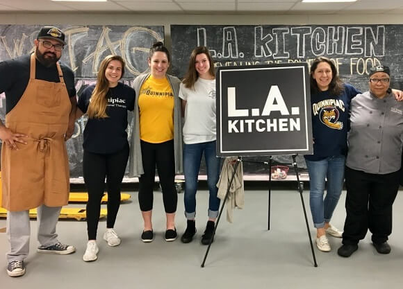 Occupational therapy students arm-in-arm at LA Kitchen in front of a LA Kitchen sign.