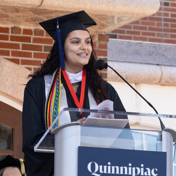 Giavanna Ragon speaks into a microphone on a Quinnipiac podium