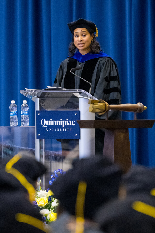 Malika Fair stands at a podium in front of dozens of medicine graduates