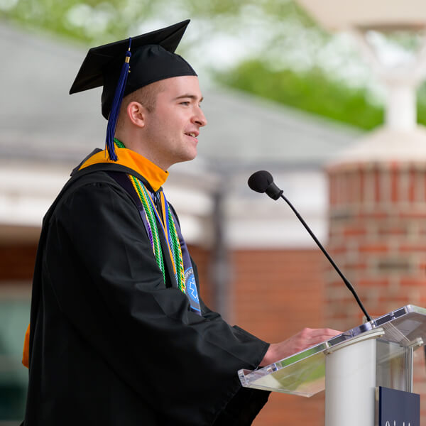 Vincent Pedulla wears a cap and gown and speaks at a podium