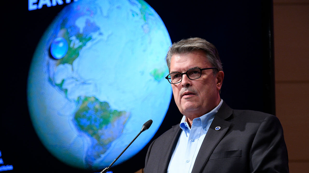 Craig McClean with an image of the world behind him speaking at the Aspen Ideas Festival