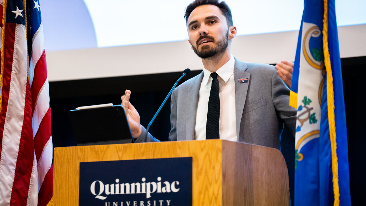 David Hogg stands at a podium and addresses the QU audience