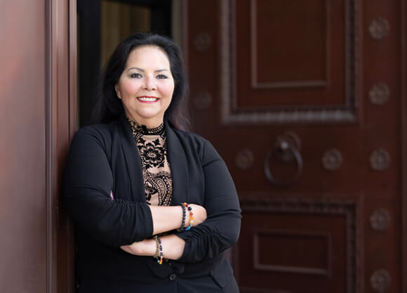 Margaret Castinado, JD '98, stands with her arms folded and smiles into the camera.