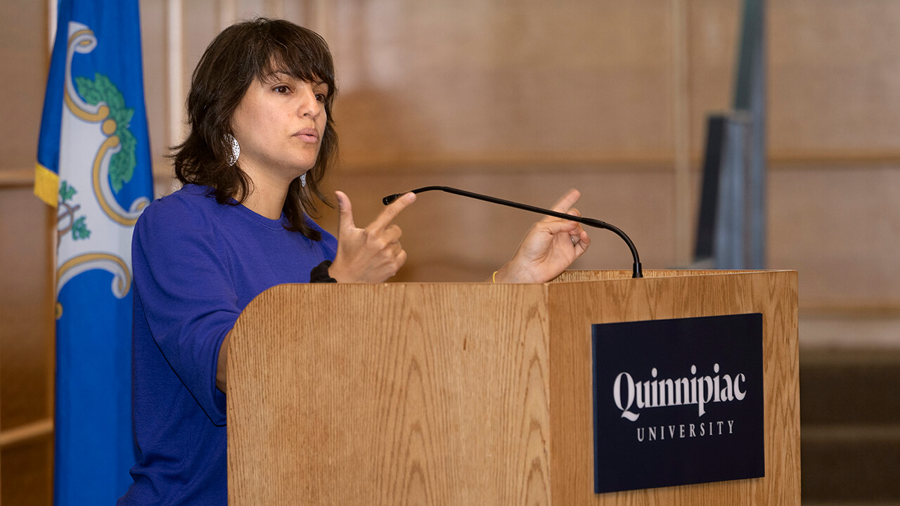 Mónica Guzmán speaks from a podium on the Quinnipiac campus